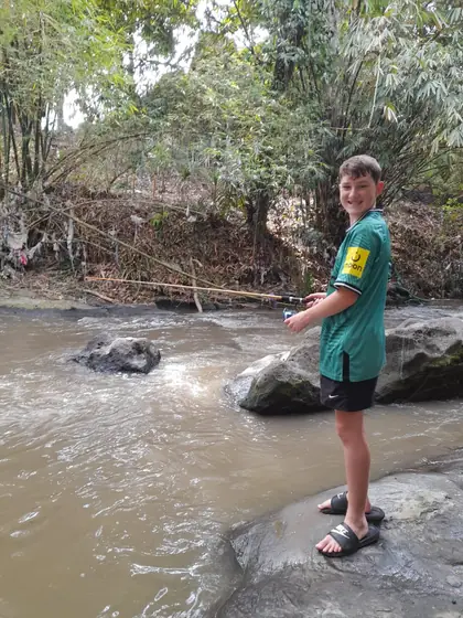 A boy standing on rocks by a river