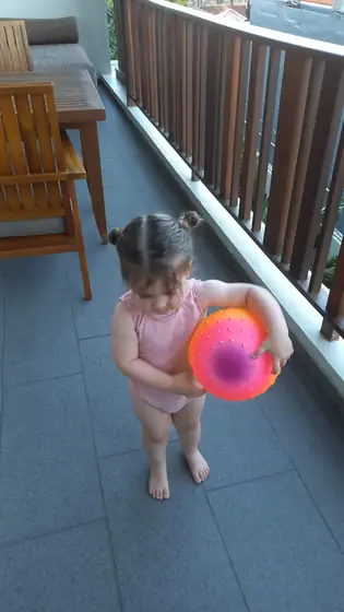 A toddler holding a ball on a balcony