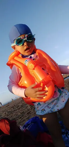 A child in a life jacket and goggles at the beach
