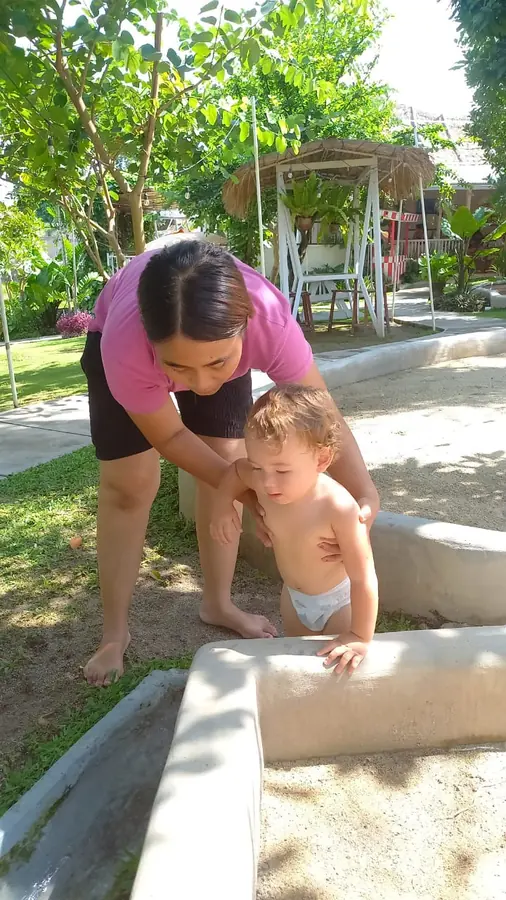 A nanny helping a toddler play in a sandpit