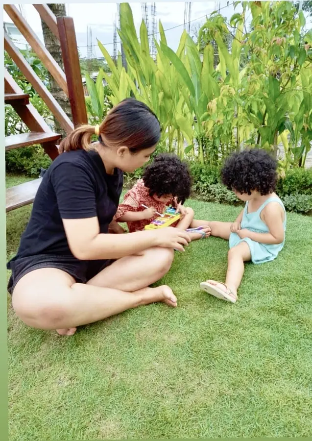 A nanny sitting on the grass playing with two small children